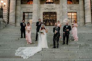 Wedding party celebrating on grand stone steps, bride and groom at center as confetti flies, bridesmaids in pink and groomsmen in black.