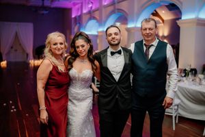 Wedding party of four posing together at elegant reception venue with purple ambient lighting.