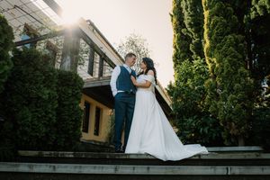 Bride and groom share a romantic moment on sunlit steps surrounded by lush greenery and cypress trees.