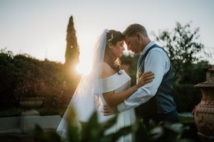 Bride and groom share romantic sunset moment, forehead to forehead, in golden backlit outdoor wedding photo.