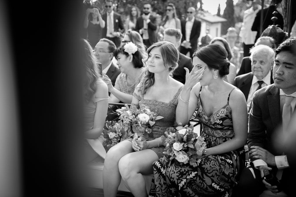 Black and white photo of emotional bridesmaids holding bouquets during an outdoor wedding ceremony.