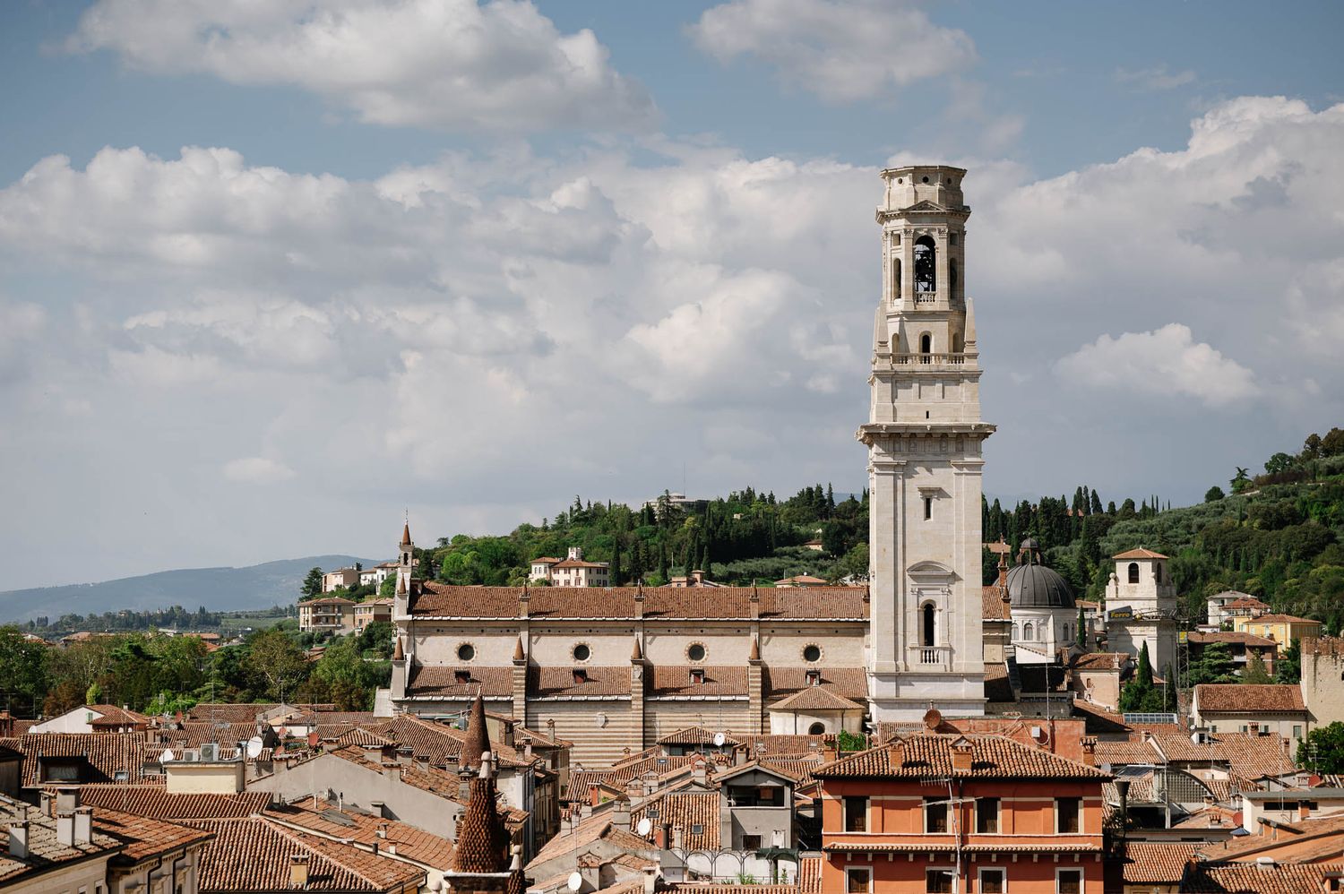 Aerial view of Verona cityscape with historic bell tower and terracotta rooftops under a partly cloudy sky.