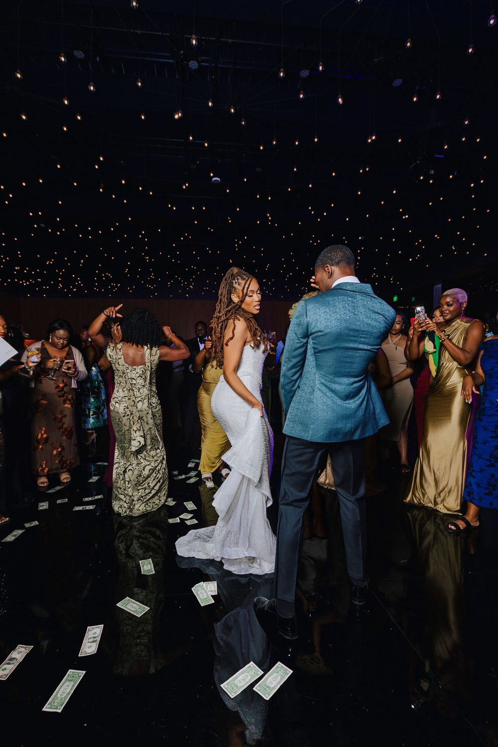 Bride and groom share first dance surrounded by guests at elegant wedding reception with twinkling star ceiling lights.