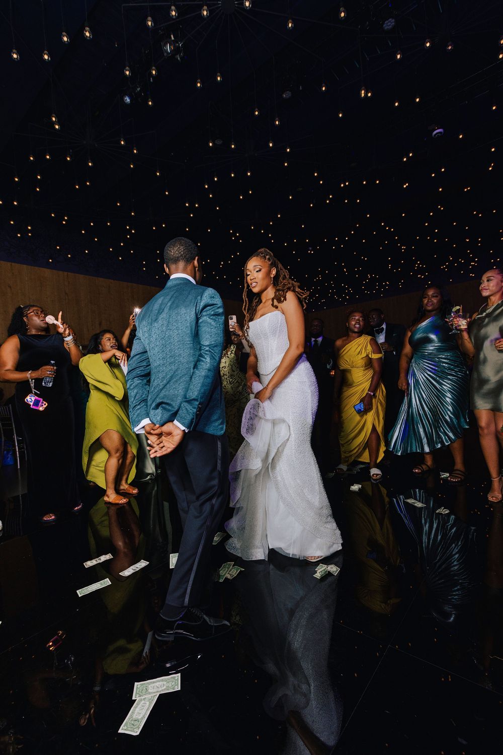Bride and groom share a dance surrounded by guests at a glamorous wedding reception with starlit ceiling.
