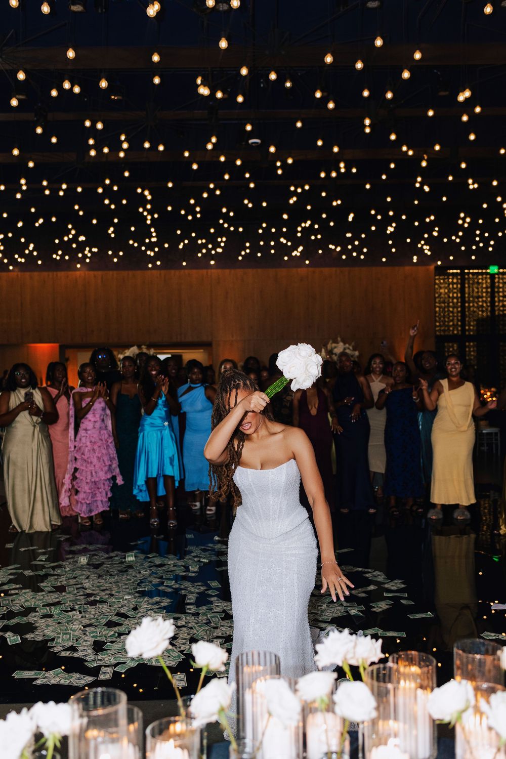 Bride in white gown prepares to toss bouquet at elegant wedding reception with twinkling ceiling lights.