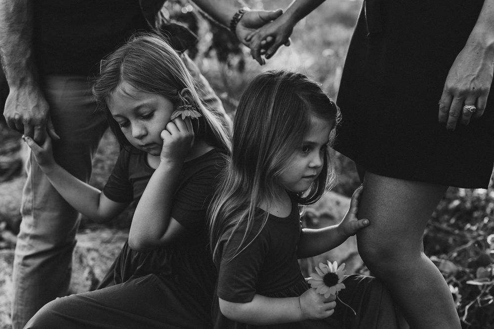 Black and white photo of two young girls crouching together outdoors, one holding a daisy flower.