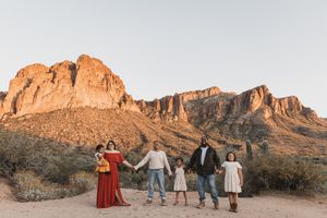 Family of five holding hands in desert landscape with Superstition Mountains glowing at golden hour in Arizona.