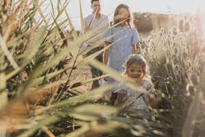 Family walking through tall grass in golden sunlight, with a smiling young girl in the foreground.