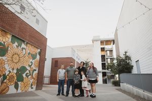 Family of six posing together in an urban courtyard beside a colorful floral mural on a brick wall.