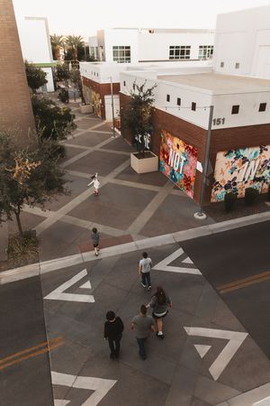 Aerial view of pedestrians walking near a colorful graffiti mural on a brick building in an urban plaza.