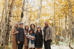 Family of seven posing together among golden aspen trees in autumn forest, smiling warmly in fall outdoor portrait.