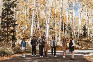 Family of six posing on a road surrounded by golden aspen trees in autumn.