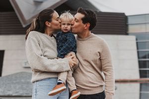 A happy young family with a toddler sharing kisses outdoors in front of a modern home.