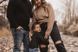 Young child hugging parents outdoors on a rocky path during a fall family photo session.