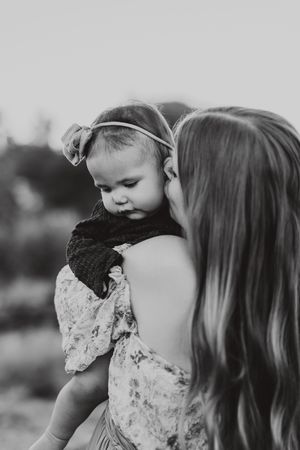 Black and white photo of a mother holding her baby girl wearing a bow headband outdoors.