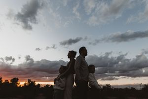Silhouette of a family of four standing back-to-back against a dramatic sunset sky with clouds.