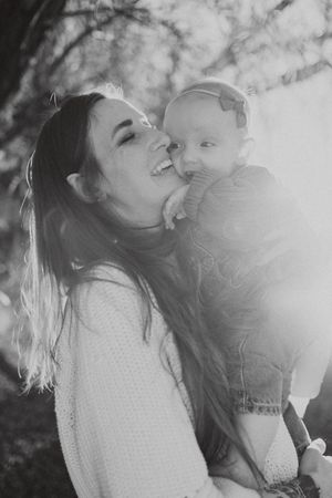 Black and white photo of a smiling mother holding her baby girl outdoors in soft natural light.