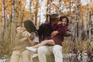 Family laughing together in autumn forest, parents hugging children among golden aspen trees in fall.