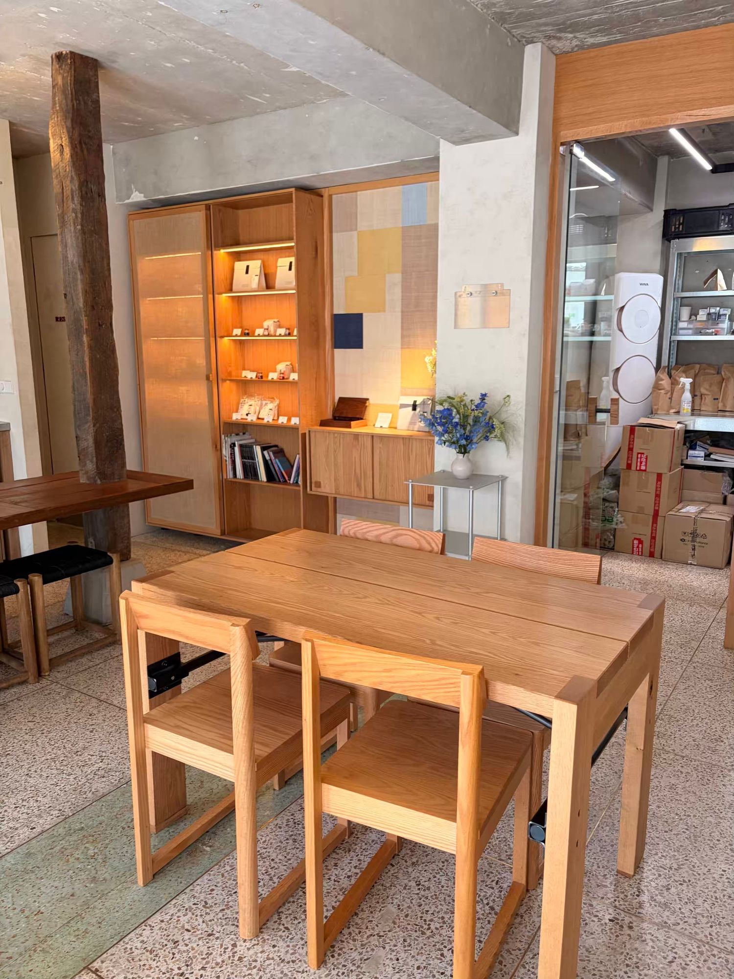 Modern wooden dining table with matching chairs in a minimalist furniture showroom with warm oak shelving.