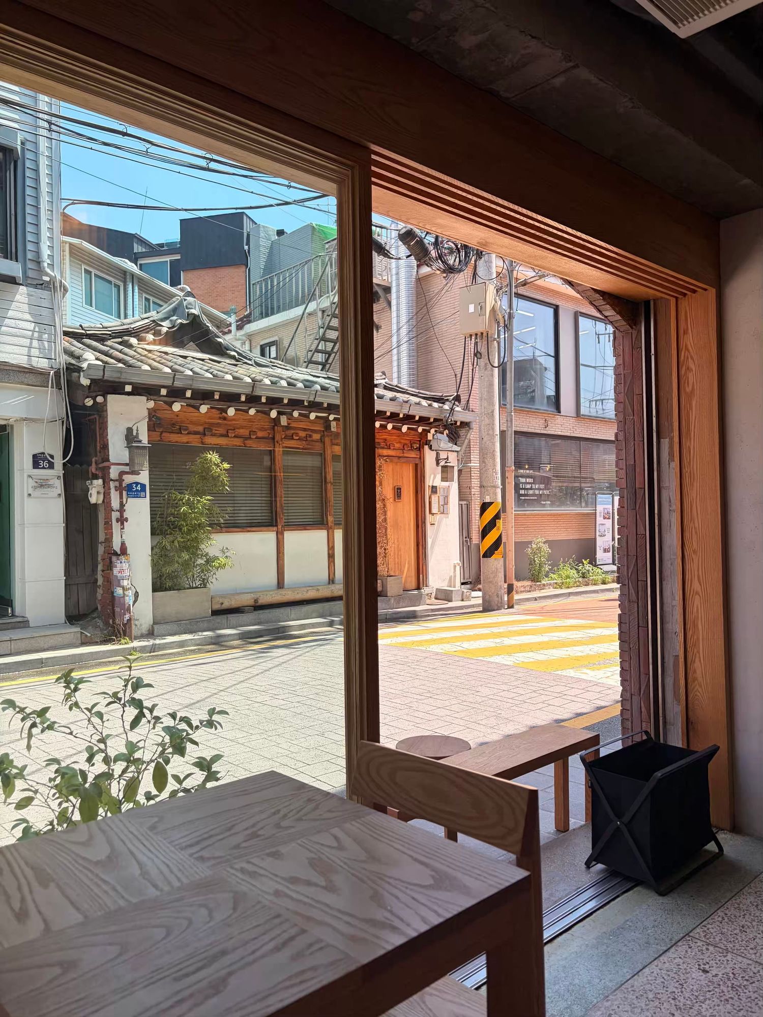 Interior view of a Korean cafe with wooden furniture overlooking a traditional hanok alley in Seoul.
