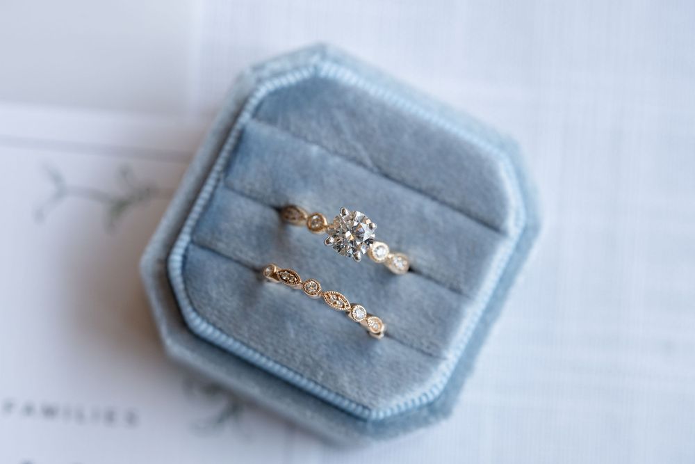 Two gold diamond rings displayed upright in a blue velvet octagonal ring box.