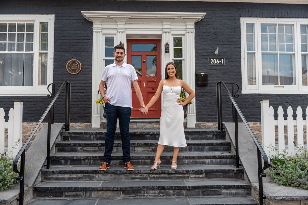 Couple holding flowers while standing on steps of a classic black and white house with a red door.