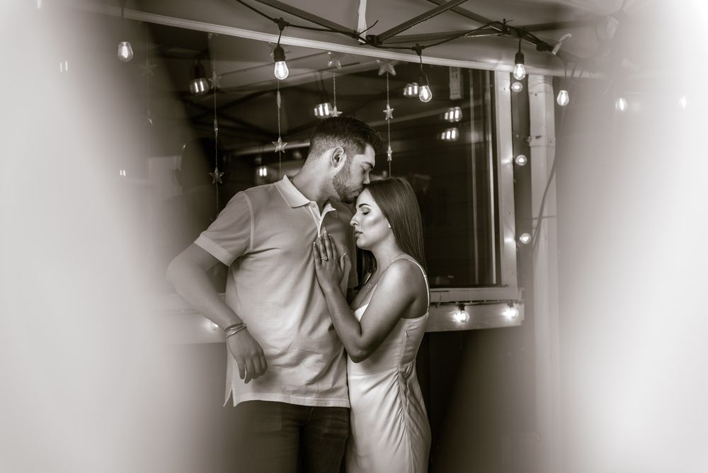 Romantic black and white photo of couple sharing a kiss under string lights in a cozy outdoor space.