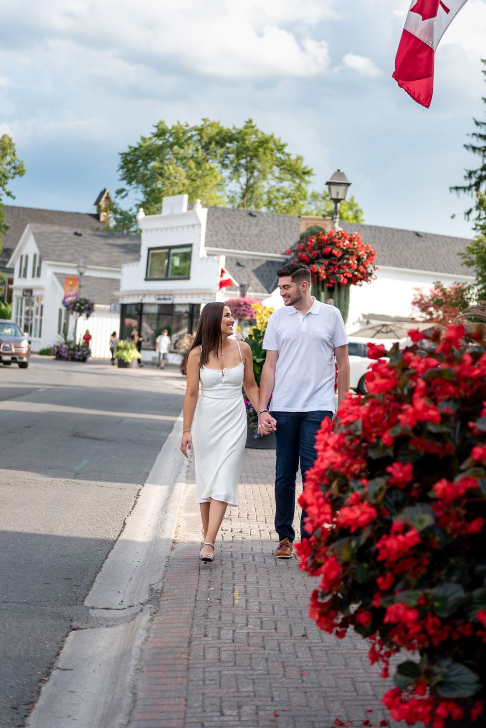 Couple walking hand in hand on a brick sidewalk with red flowers and Canadian flag.