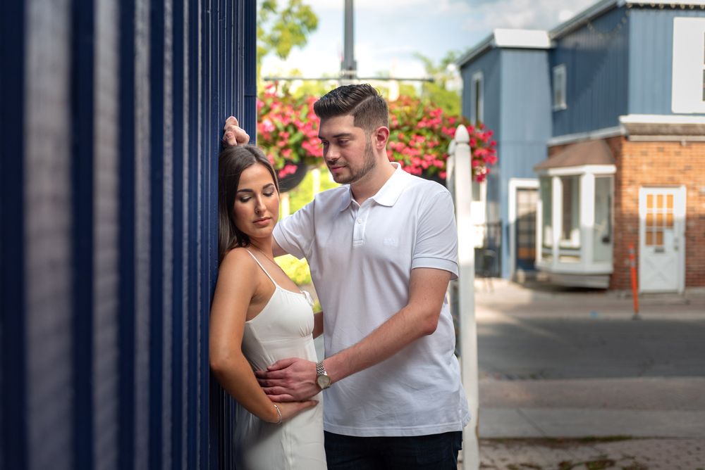 Couple embracing near a blue wall with pink flowers, woman in white dress and man in white polo shirt.