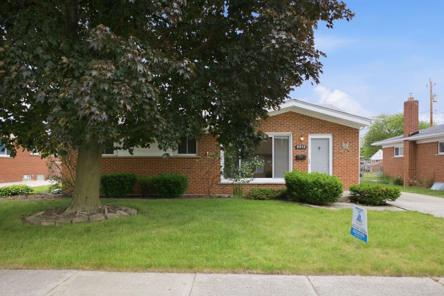 Charming brick ranch home with white trim, covered front porch, and detached garage amid autumn trees.