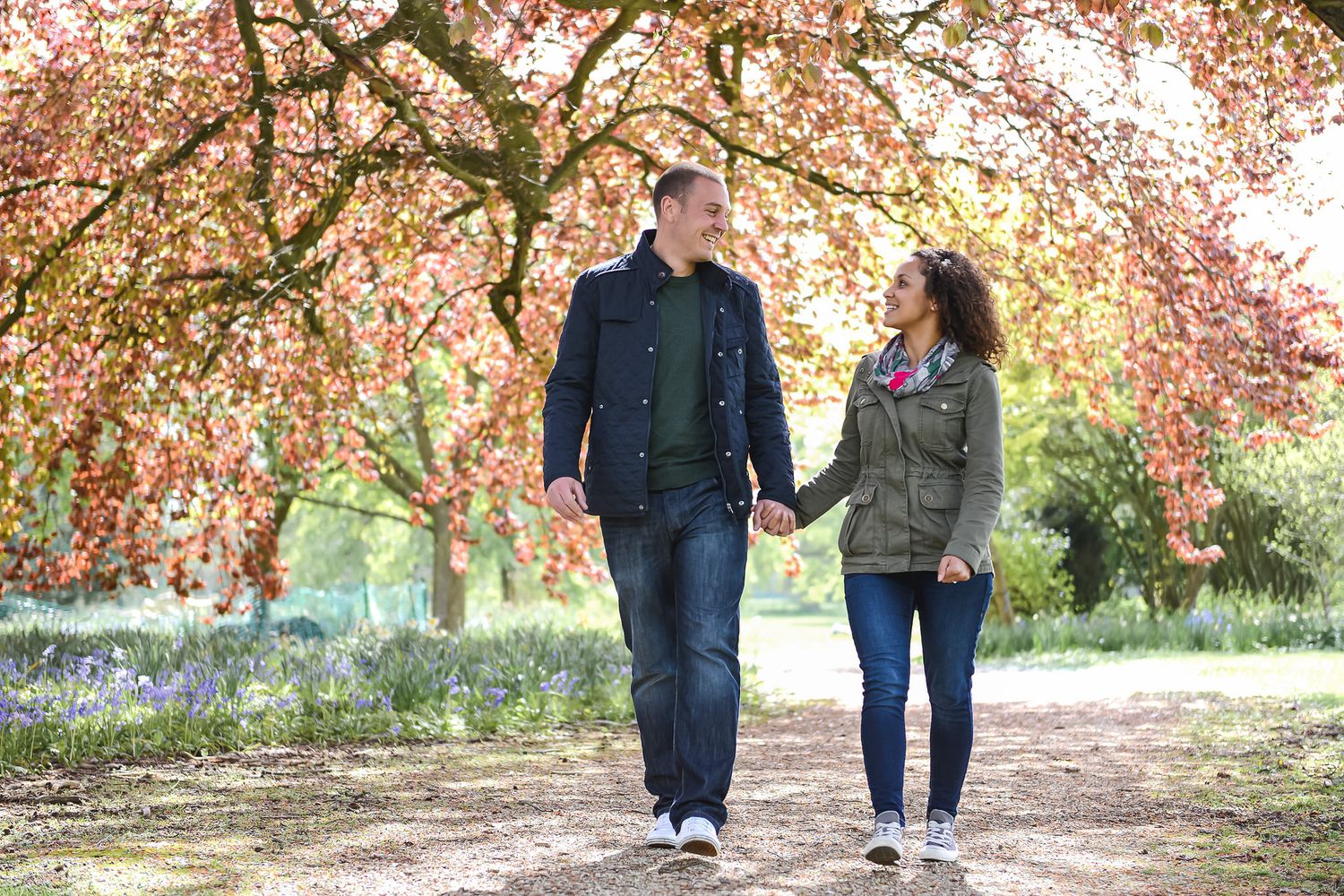 Couple holding hands walking through autumn park with colorful red and orange trees on a sunny day.