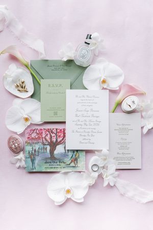 Elegant wedding invitation suite with sage green envelopes, save the date, and white orchids on a soft pink background.