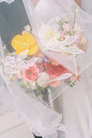 Close-up of a colorful bridal bouquet with pink, yellow, and coral flowers draped under an embroidered wedding veil.