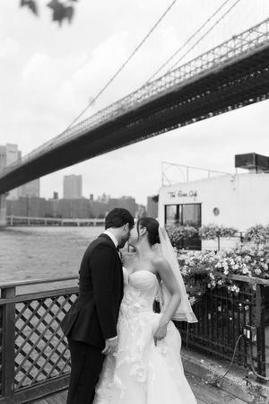 Black and white photo of bride and groom kissing near Brooklyn Bridge waterfront at The River Cafe wedding venue.