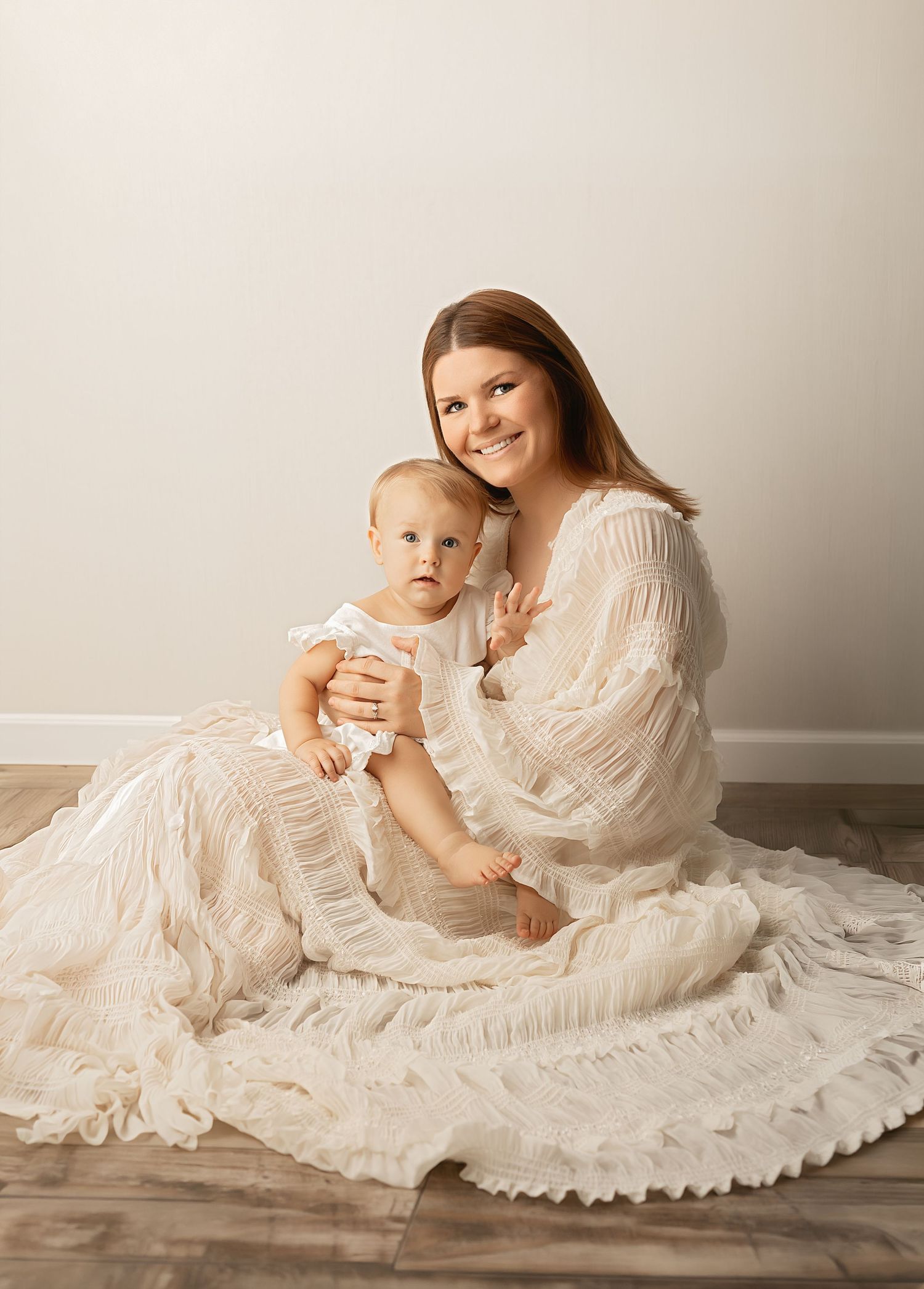 Black and white photo of a pregnant woman in a white ruffled dress sitting on a wooden dock.