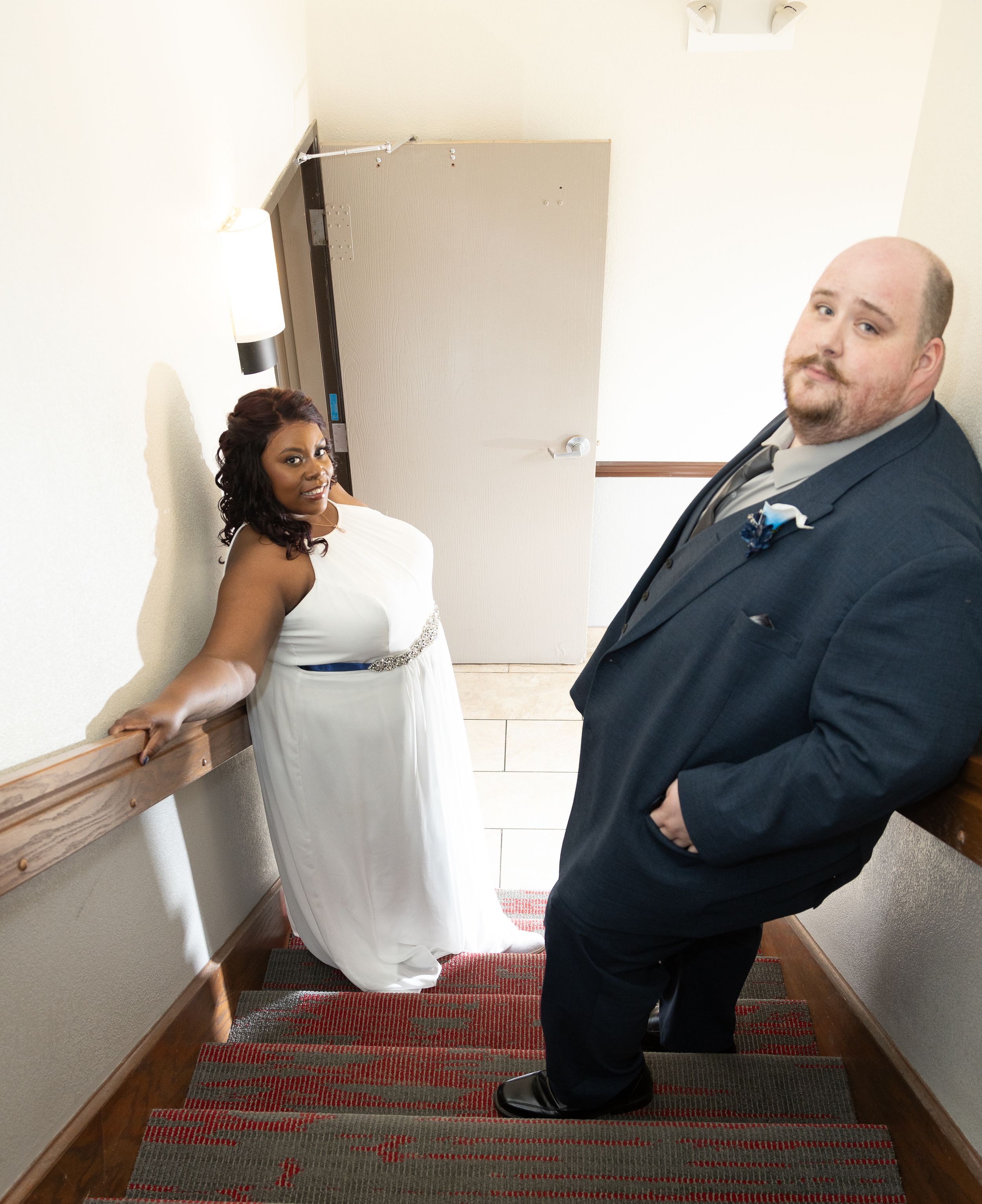 Bride in white gown and groom in dark suit pose on carpeted staircase during wedding day portrait.
