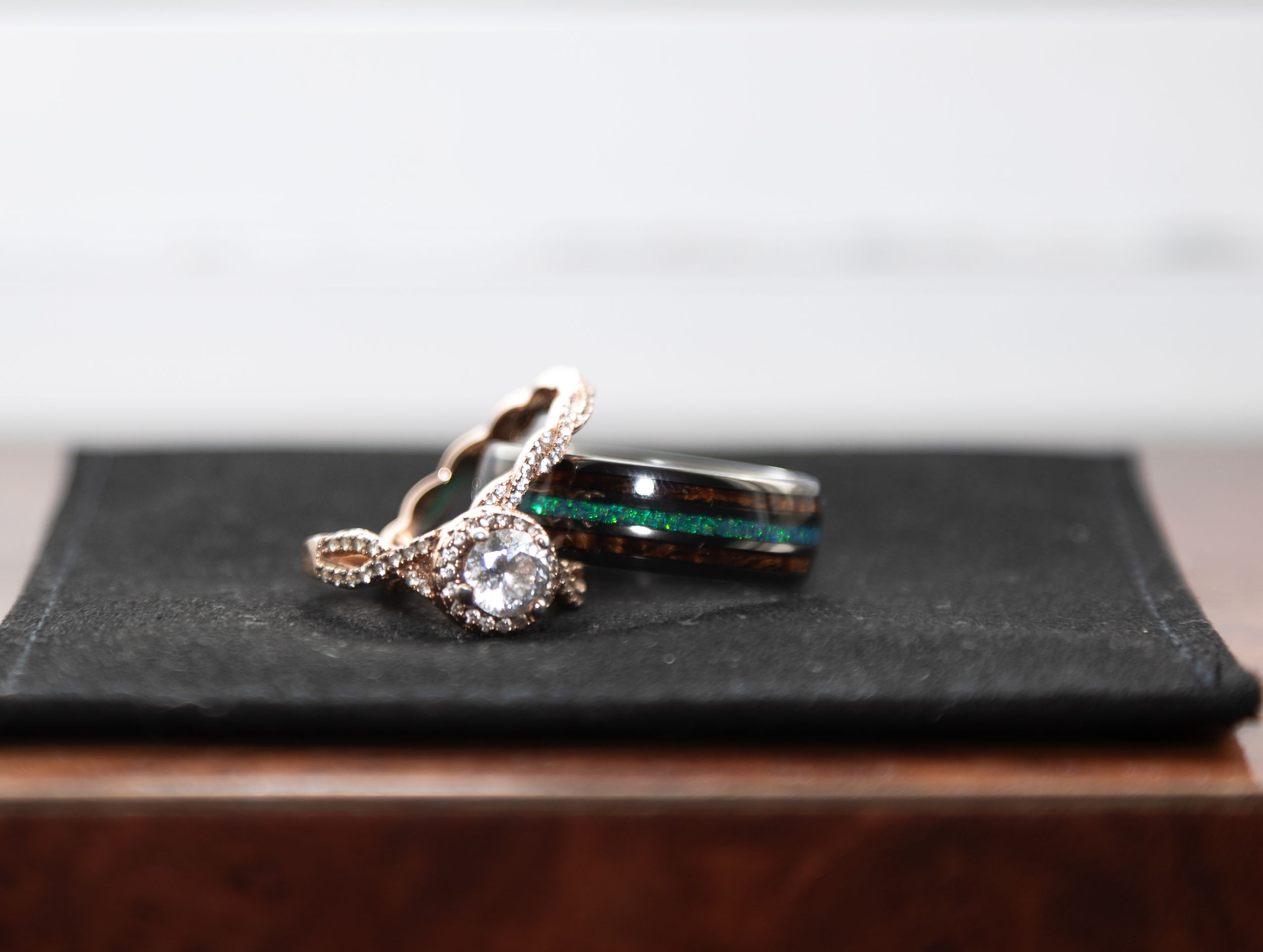 Three elegant rings on a dark velvet pad, featuring a diamond engagement ring and teal inlay wedding bands.