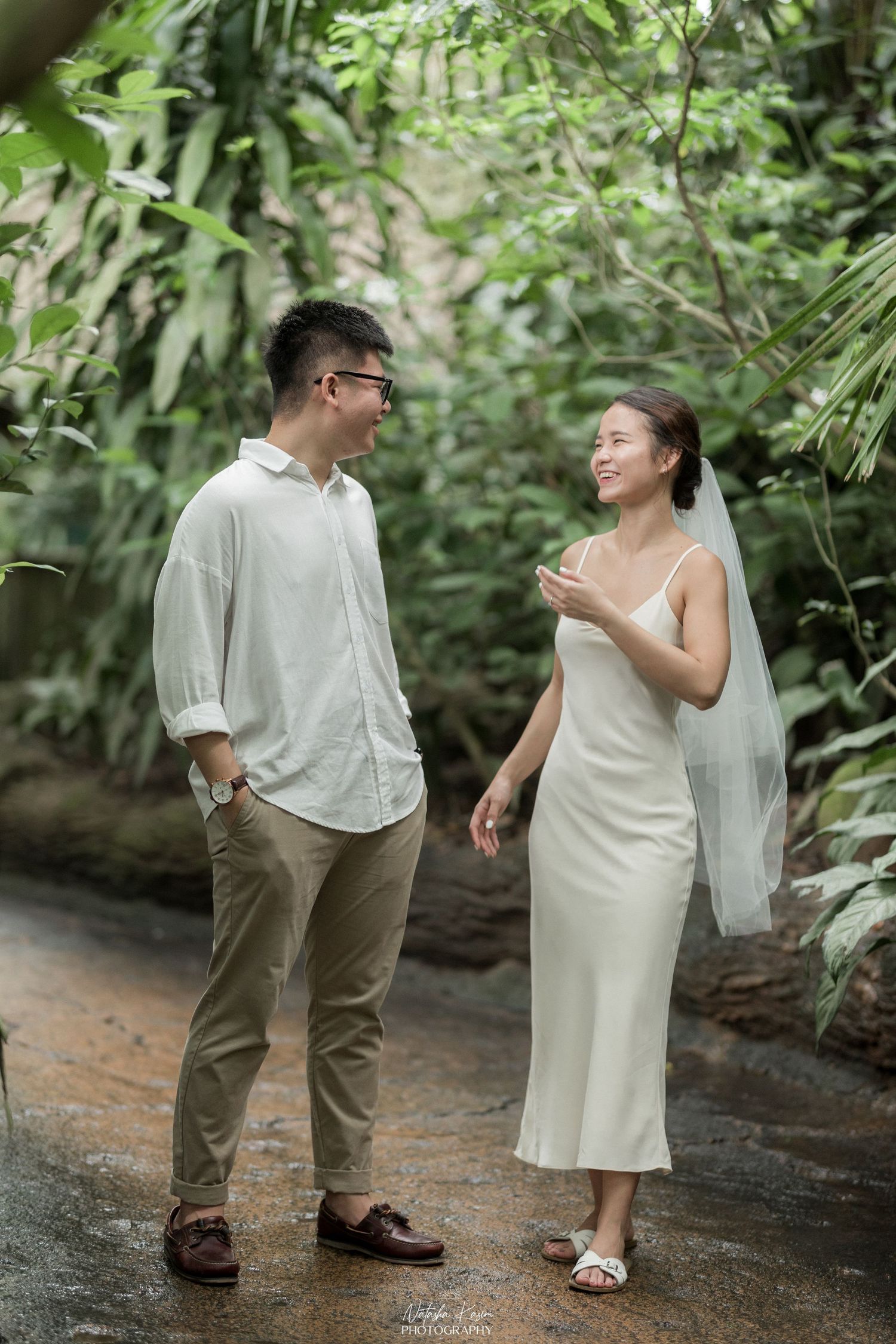 A couple walking along a brick pathway surrounded by manicured gardens and trees.