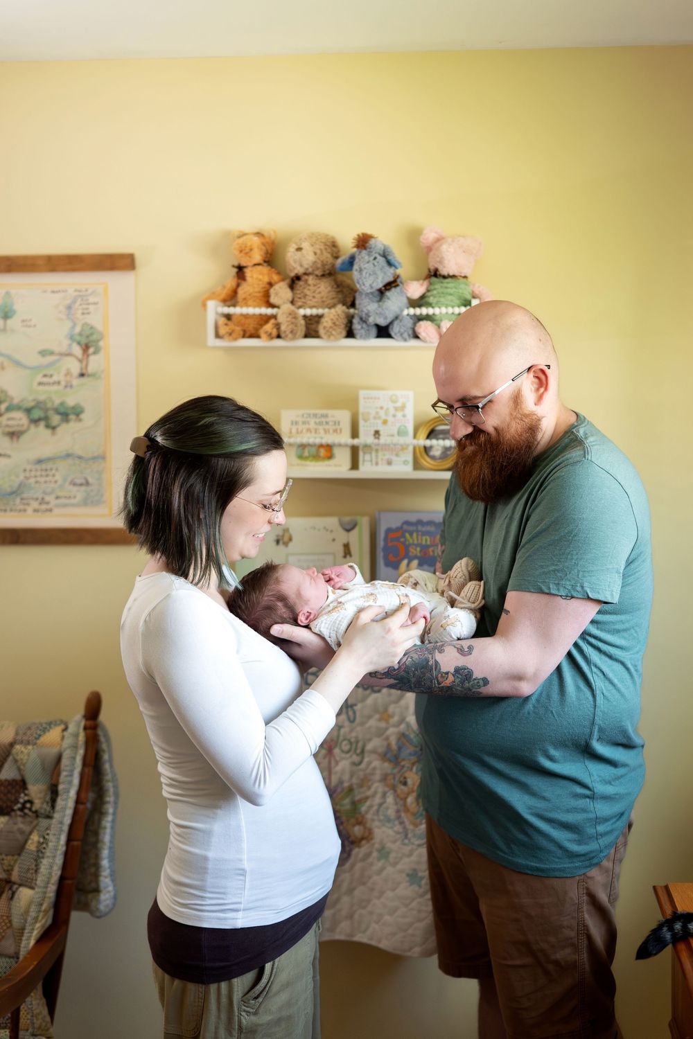 New parents lovingly hold their newborn baby in a warmly decorated nursery with stuffed animals.
