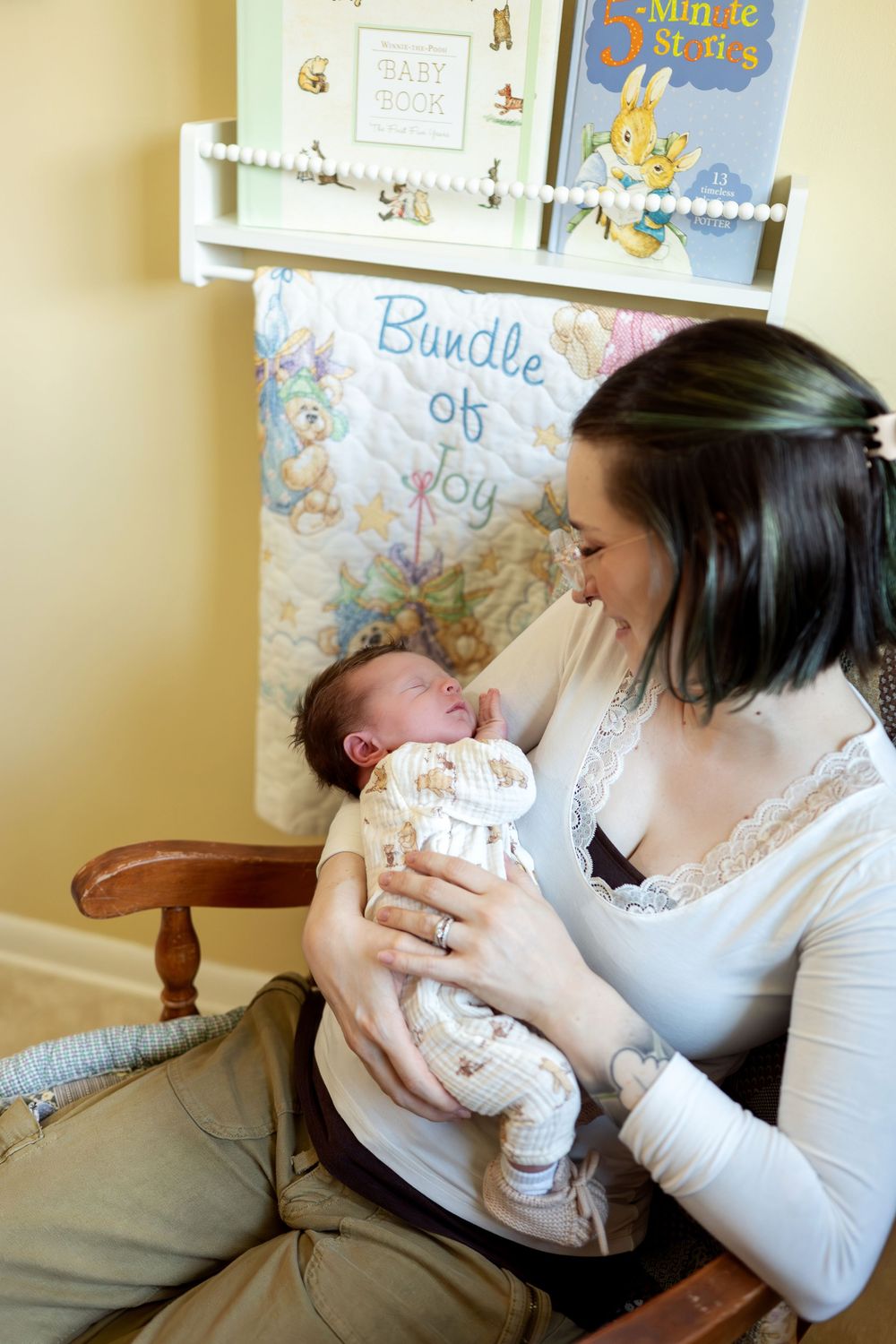 A new mother smiles lovingly at her alert newborn baby in a cheerful yellow nursery room.