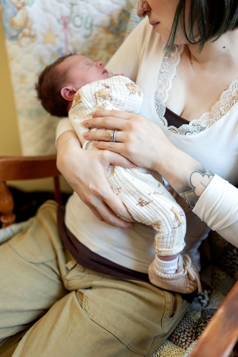 A close-up of a mother in a white lace top carefully cradling her swaddled newborn baby.
