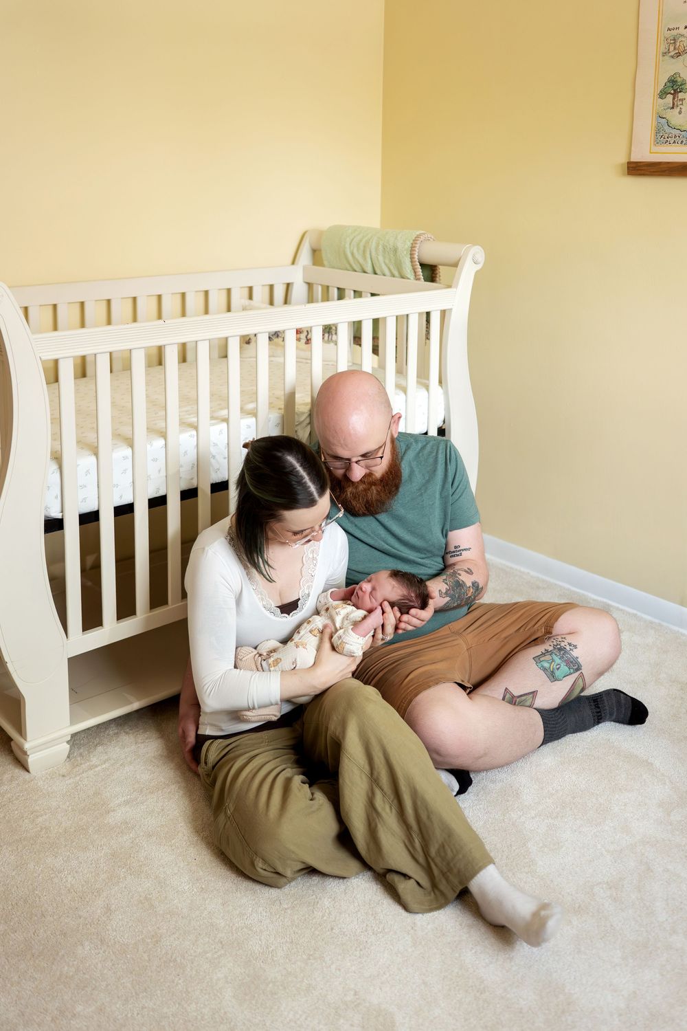 New parents sitting together on nursery floor admiring their newborn baby.