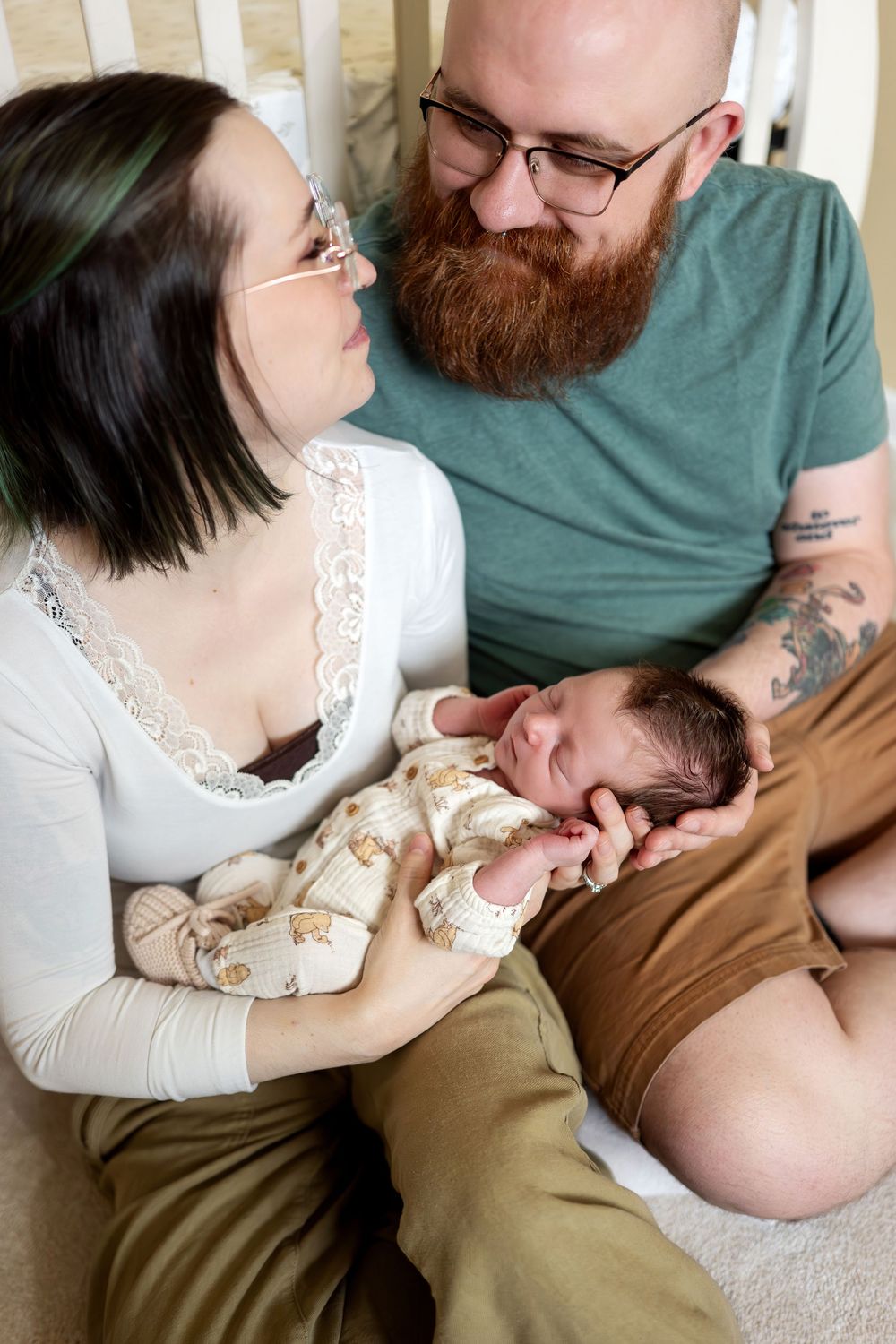Close-up of new parents with glasses smiling at newborn baby in nursery.