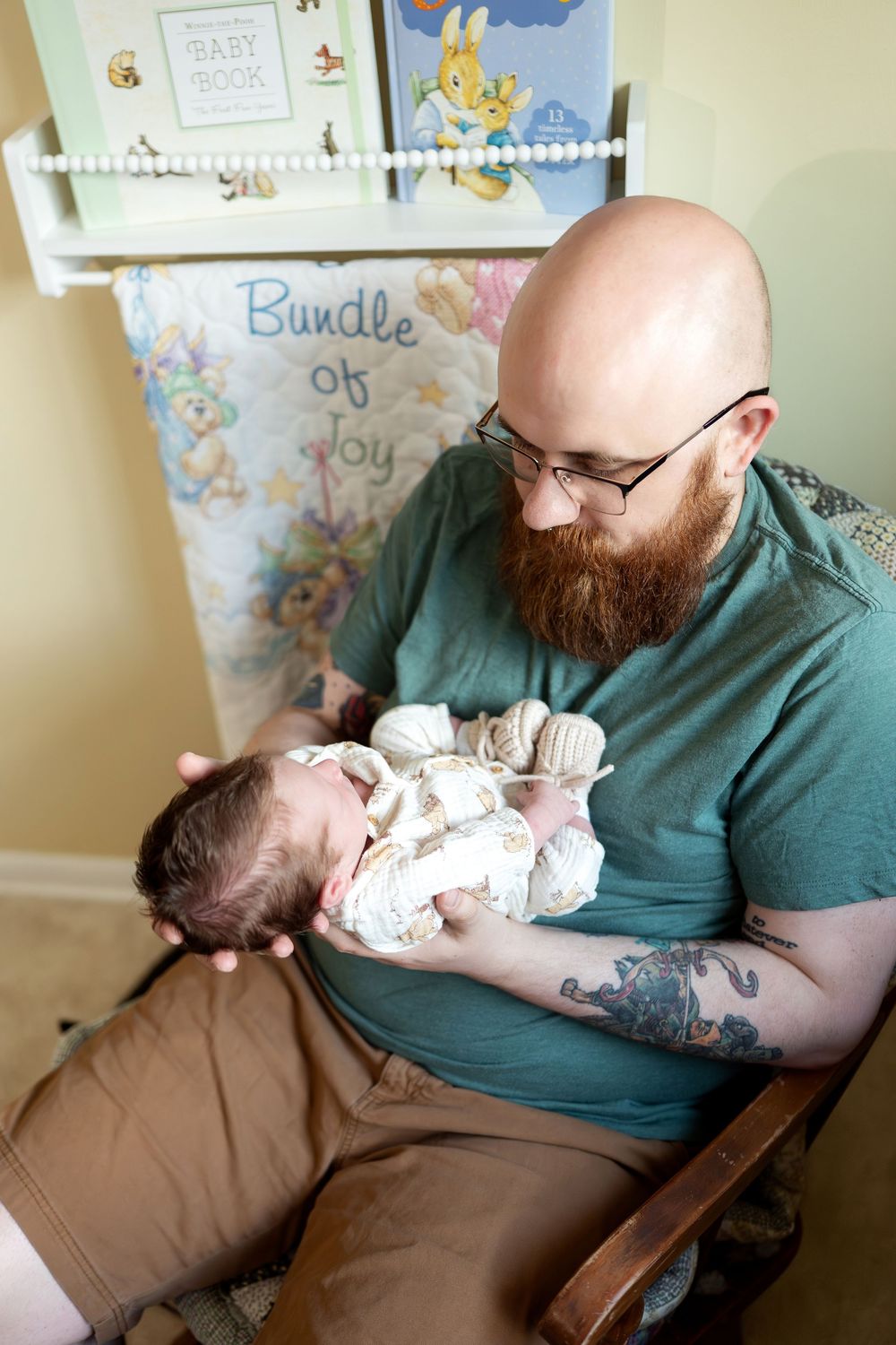 Overhead view of bald bearded father holding newborn baby in front of Bundle of Joy nursery decor.
