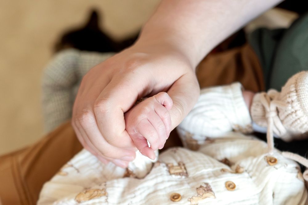 Adult hand gently holding tiny newborn baby fingers in close-up detail shot.