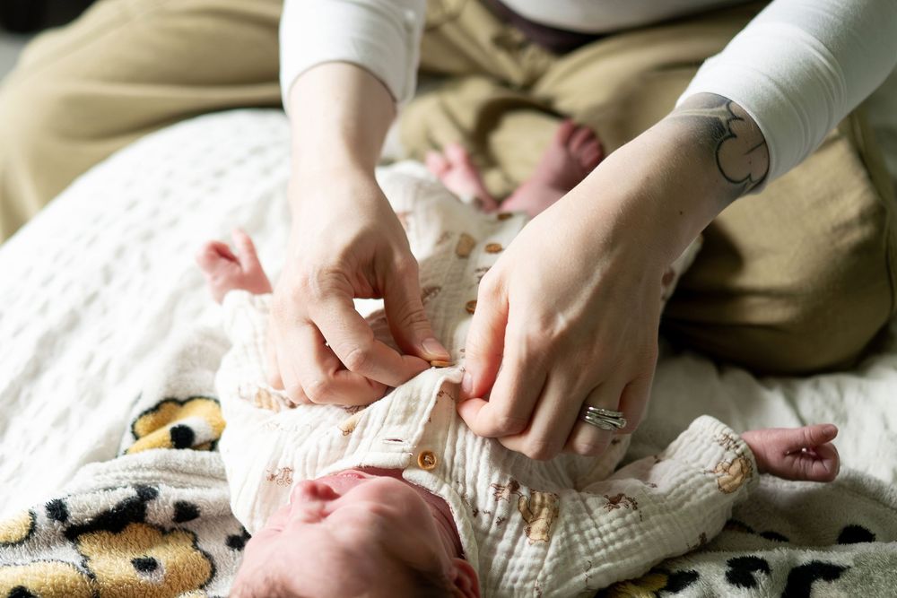 Mothers hands carefully dressing newborn baby lying on floral blanket on bed.
