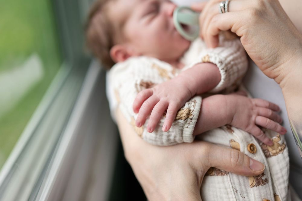 Close-up of newborn baby hands with pacifier in mothers arms.