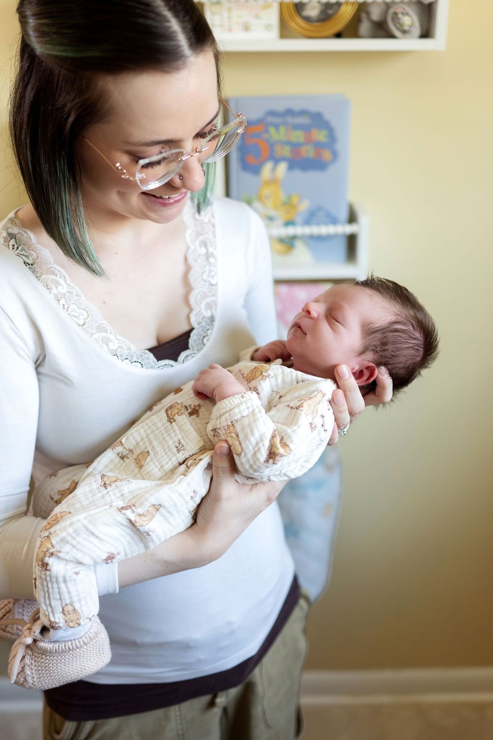 Happy mother with glasses smiling at her newborn baby wrapped in cream patterned swaddle blanket.