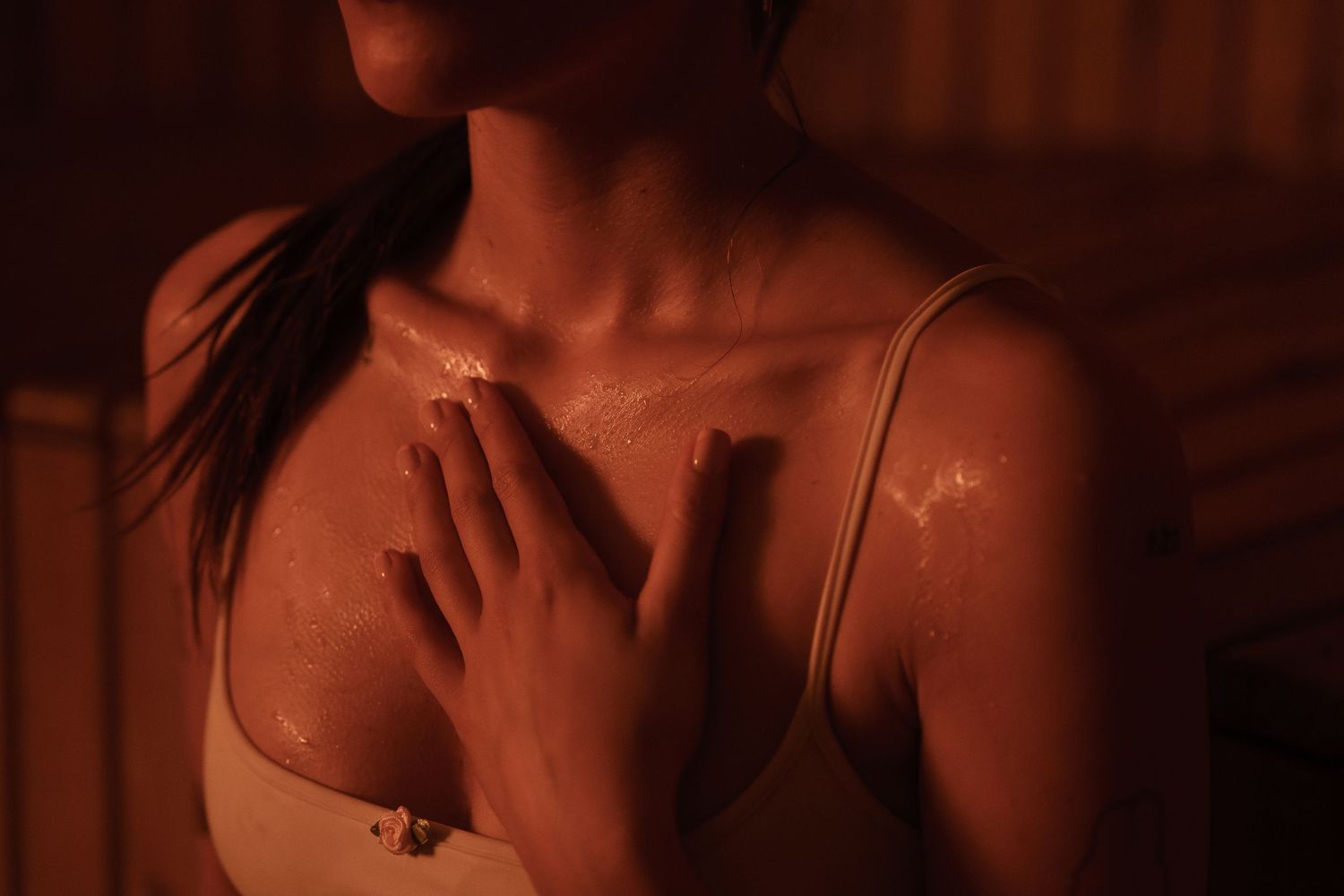 Woman in beige top applying skincare in warm amber sauna light, skin glowing with moisture.