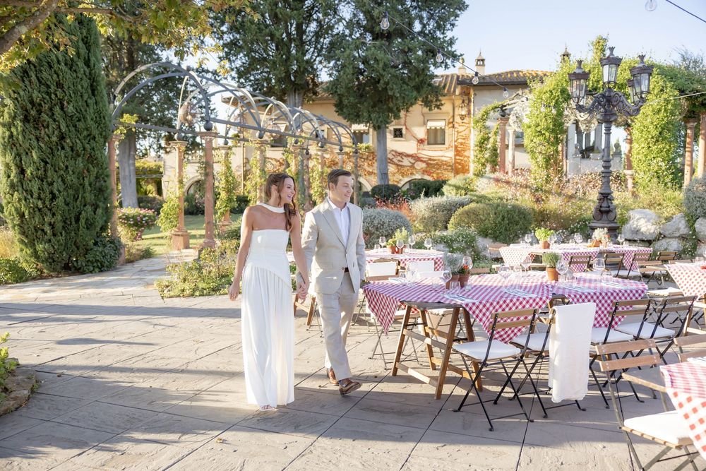 Bride and groom walk hand-in-hand at an outdoor wedding reception with elegant table settings and lush greenery.